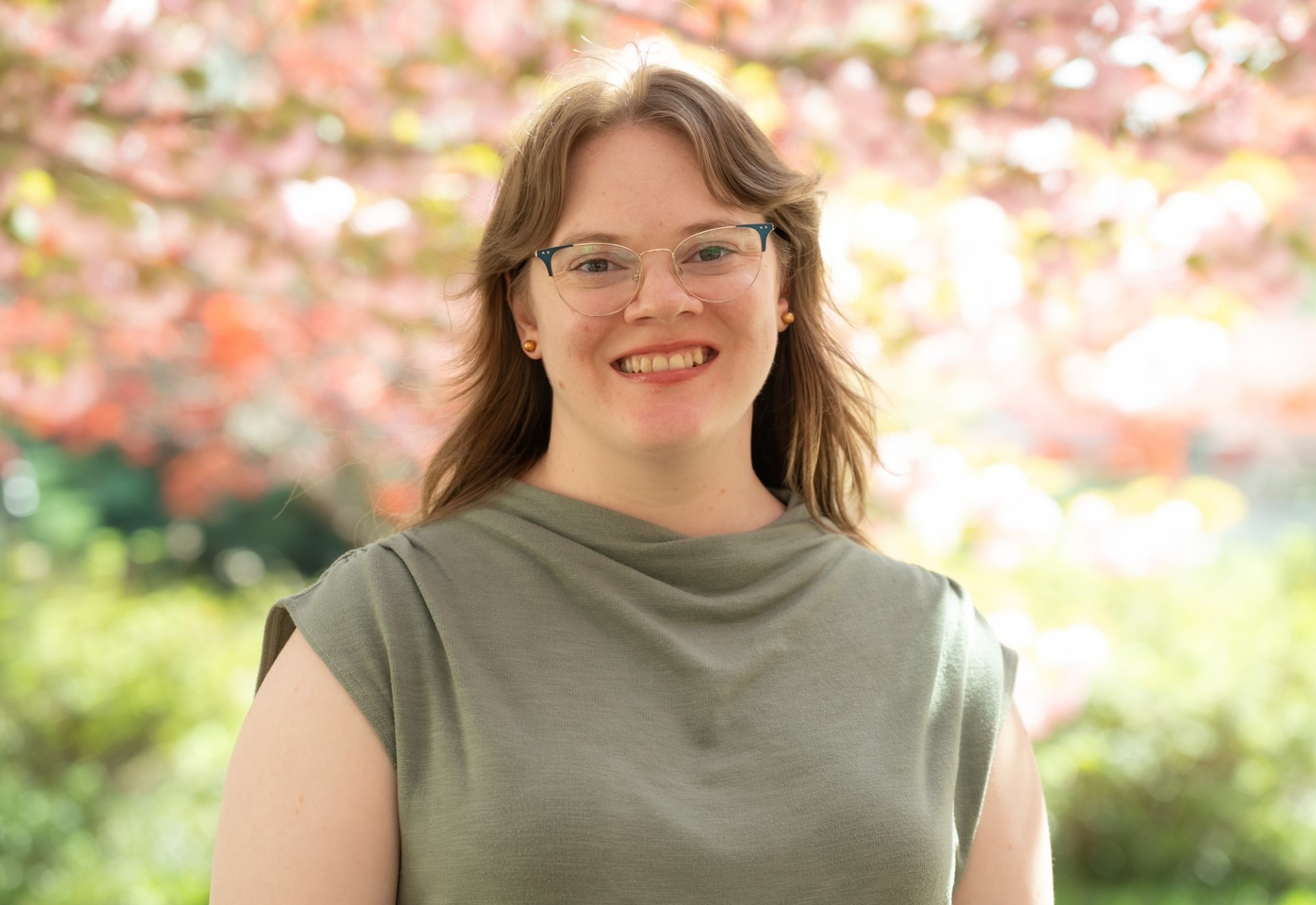 A woman wearing glasses smiling against a backdrop of plum blossoms.