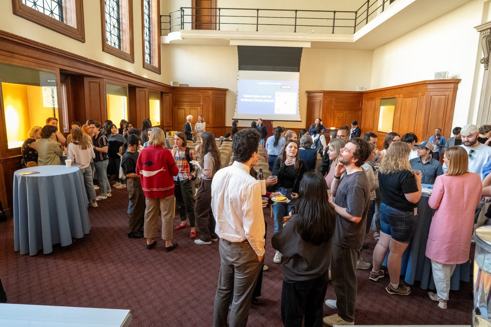 After the presentations, audience members take a break while the judges confer. Audience members talking and eating food while standing and at tables.