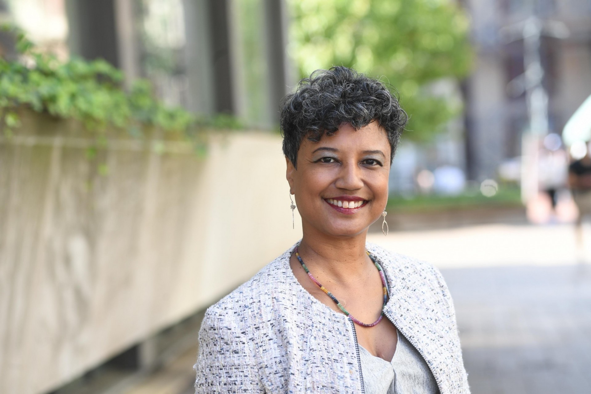 woman with short hair smiling in front of background of concrete and green plants