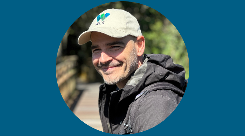 A man in a parka and a baseball cap smiles for a protrait.