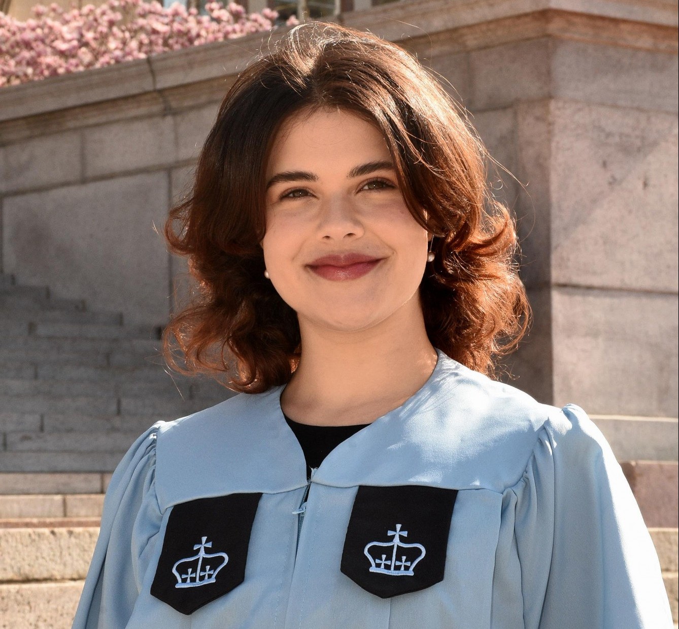 A woman in a graduation gown smiles at the camera.
