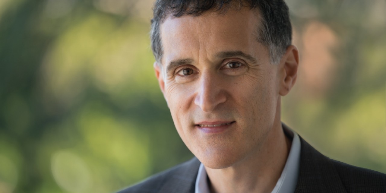 A close-up headshot of a man with short black hair.