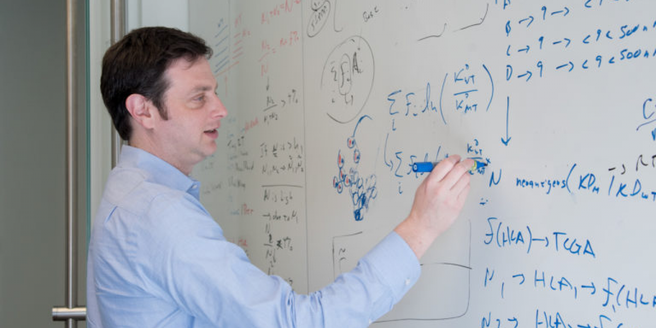 A man writes a formula on a whiteboard.