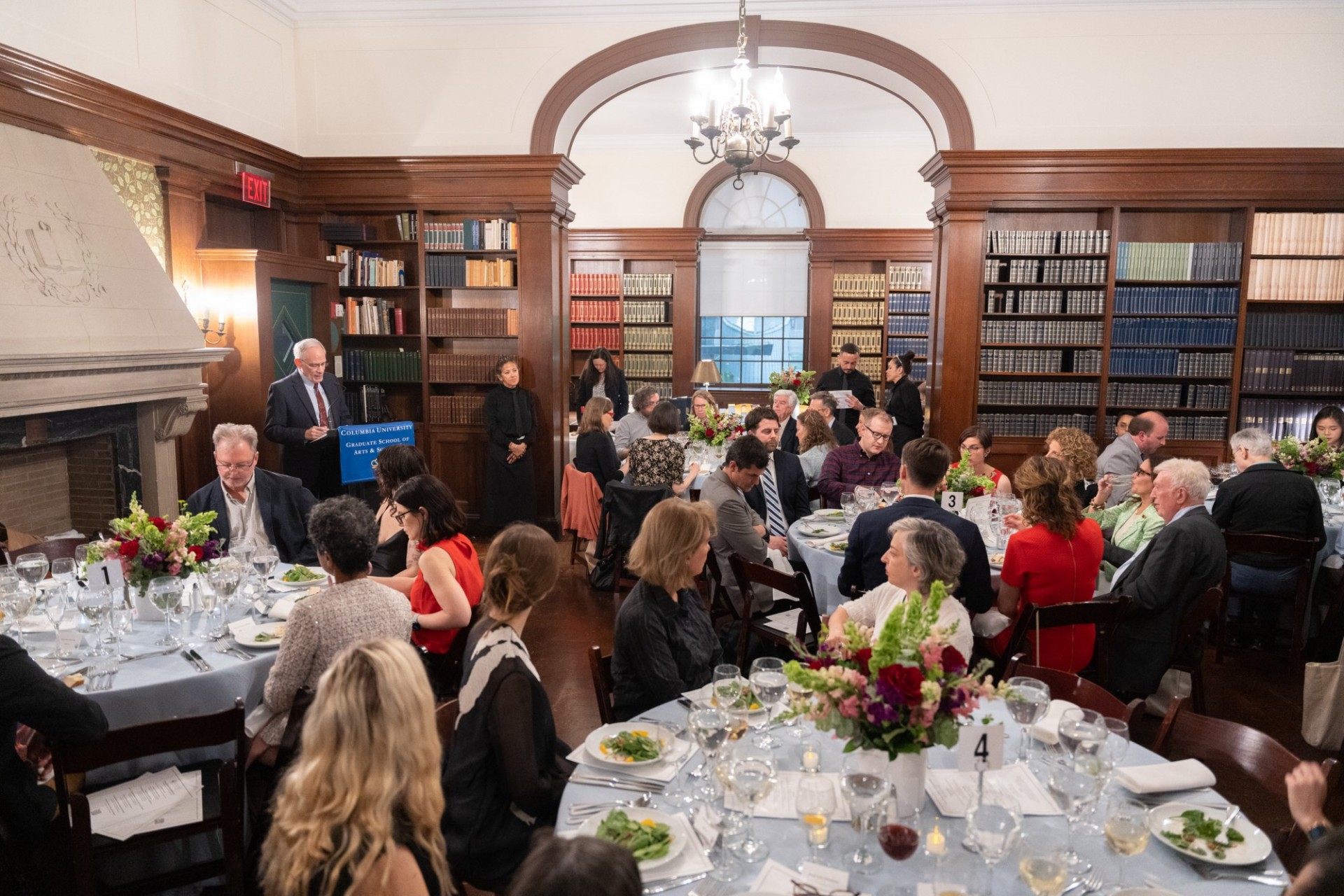 Dean Carlos Alonso giving opening remarks in the library of Casa Italiana Room full of people at tables, celebrating