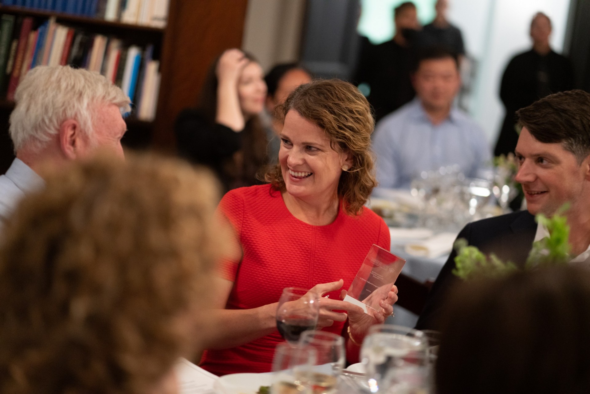 People seated at dinner table, woman smiling, holding award