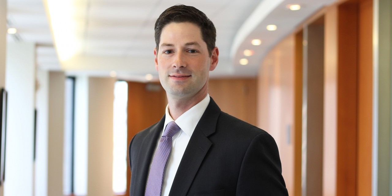A portrait of a man in a suit in an office hallway.