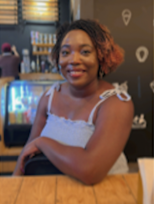 Darker brown-skinned person with chin-length two-toned dark and reddish hair, smiling into camera.