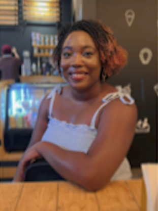 Darker brown-skinned person with chin-length two-toned dark and reddish hair, smiling into camera. 