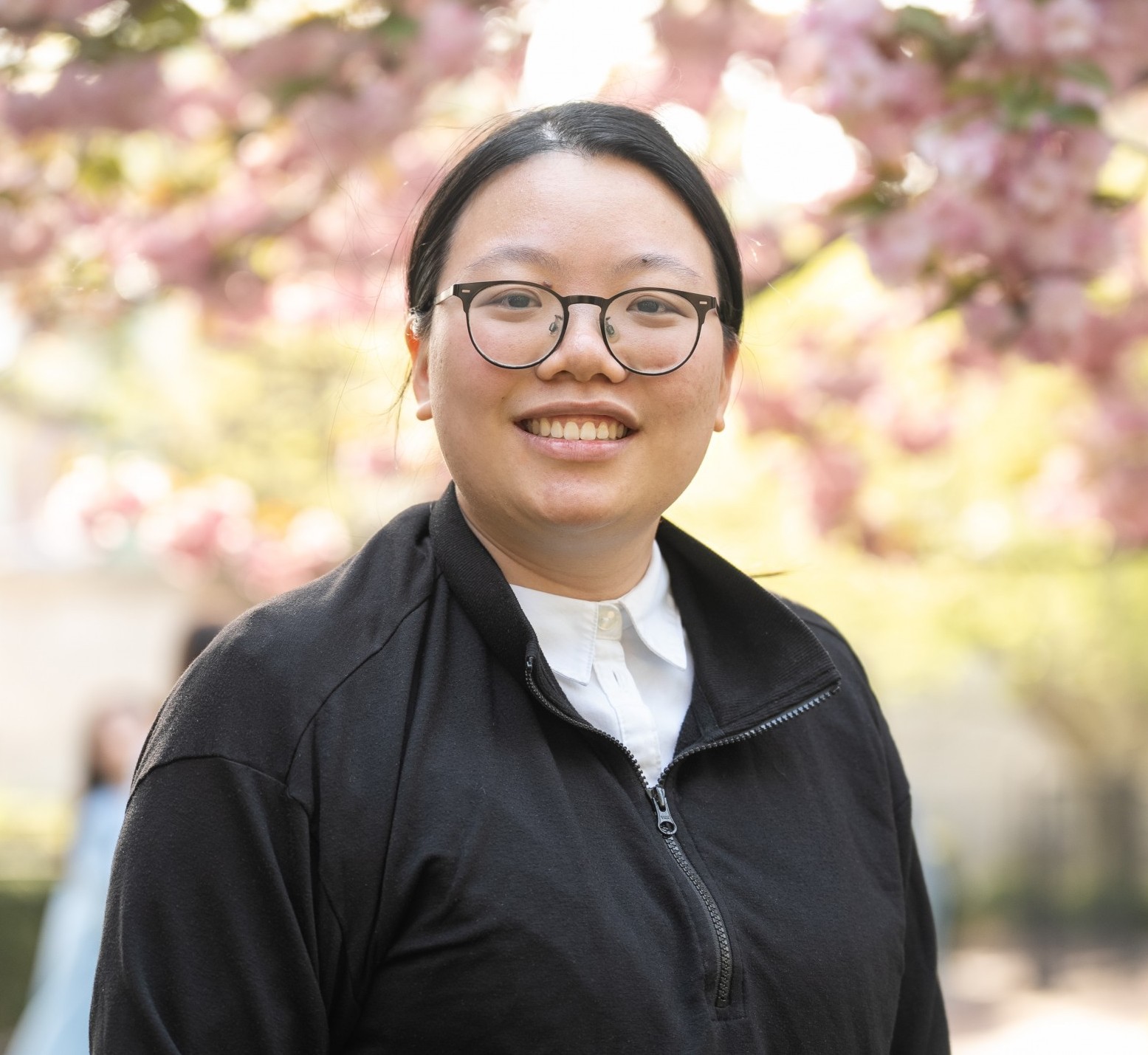 A woman with glasses smiling in front of a flowering tree.