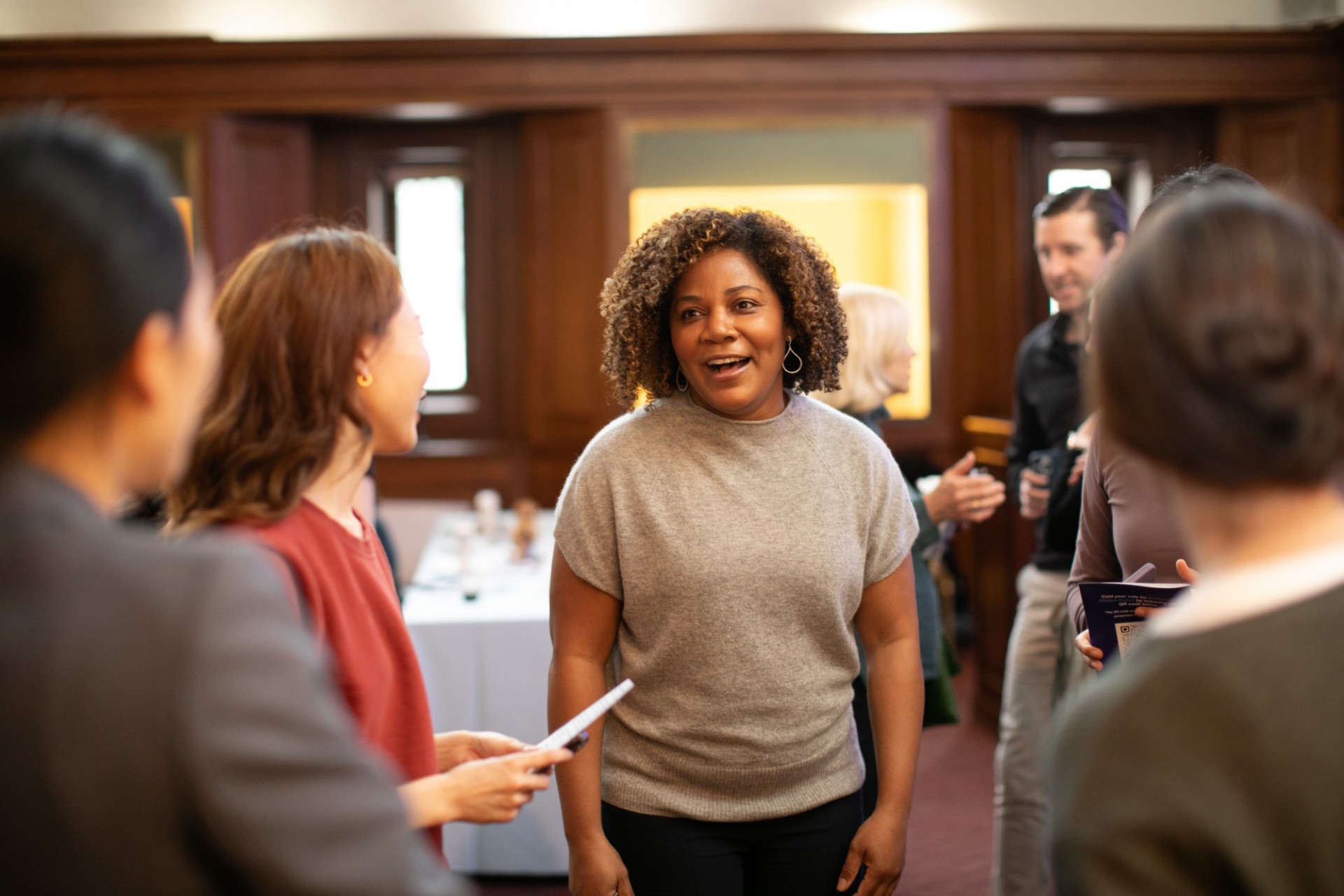 Natalie Greaves-Peters (TC) post-presentation, relieved Students socializing after speeches, Black woman with curly hair and grey shirt standing in middle
