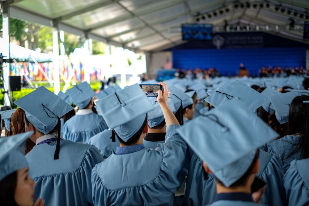 A graduate snaps a photo during the opening remarks. A graduate snaps a photo during the opening remarks.