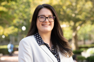 Woman with long brown hair and glasses smiling to camera