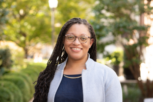 Head and shoulders of woman with glasses and dark skin and long dark hair smiling to camera