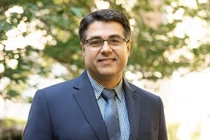 Amirreza Barin Head and shoulders of man with light skin, glasses, dark hair, in dark suit jacket and light blue button shirt smiling to camera.