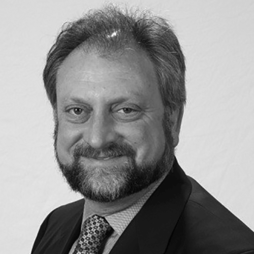 A black and white headshot of a man in a suit smiling.
