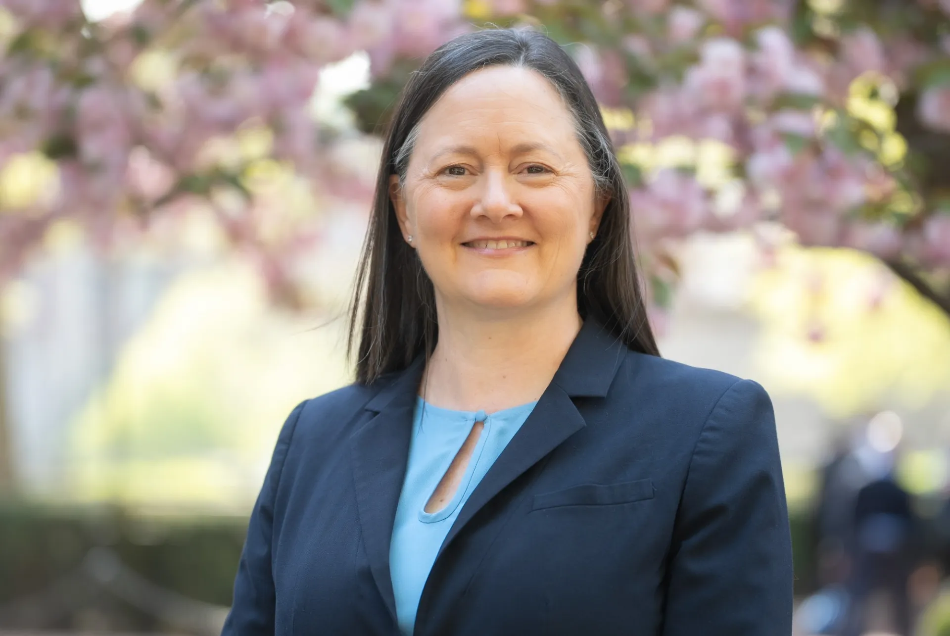 Portrait of woman in a blue blazer smiling against a plum blossom tree.