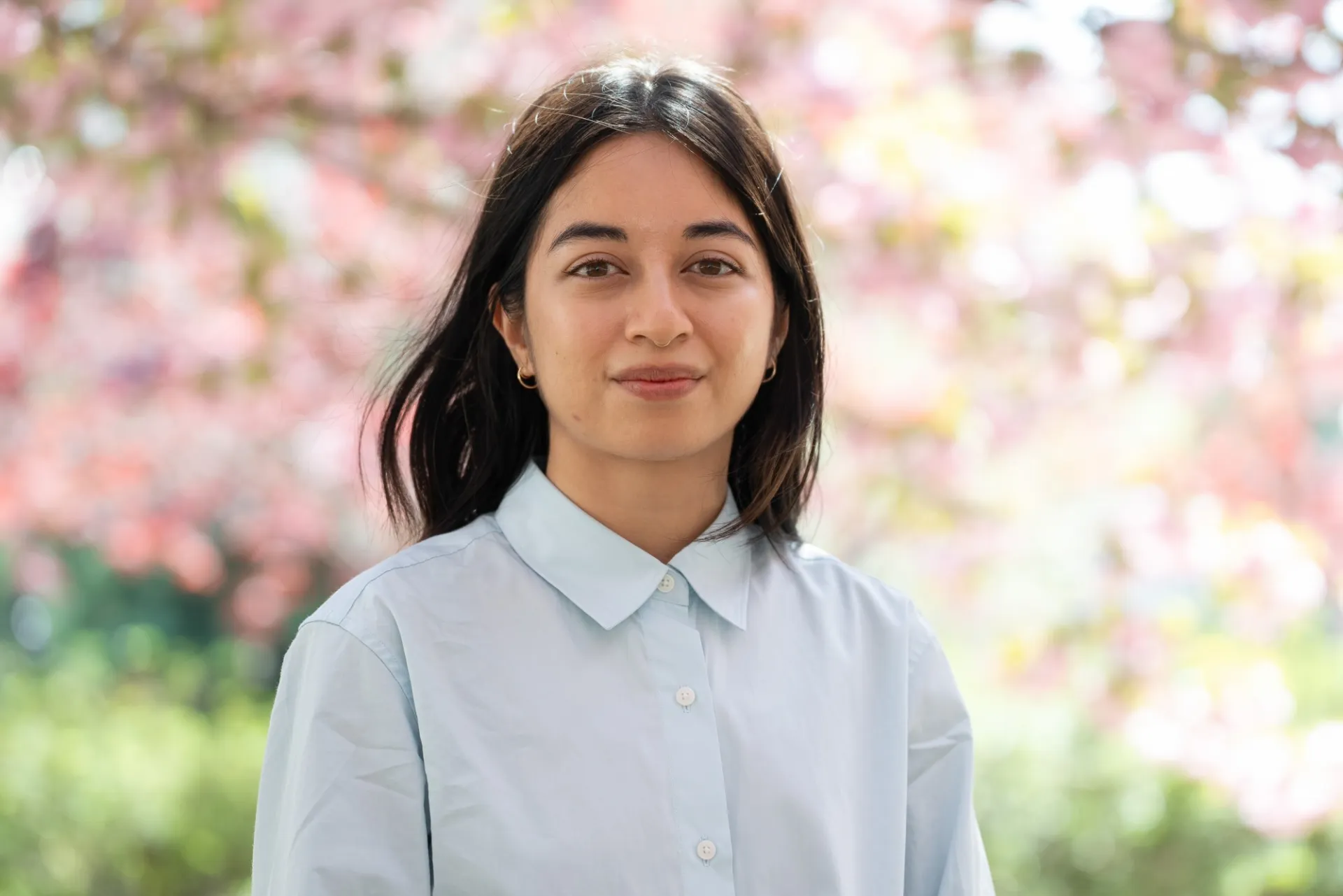A woman in a light blue button-up against a backdrop of cherry blossom trees.