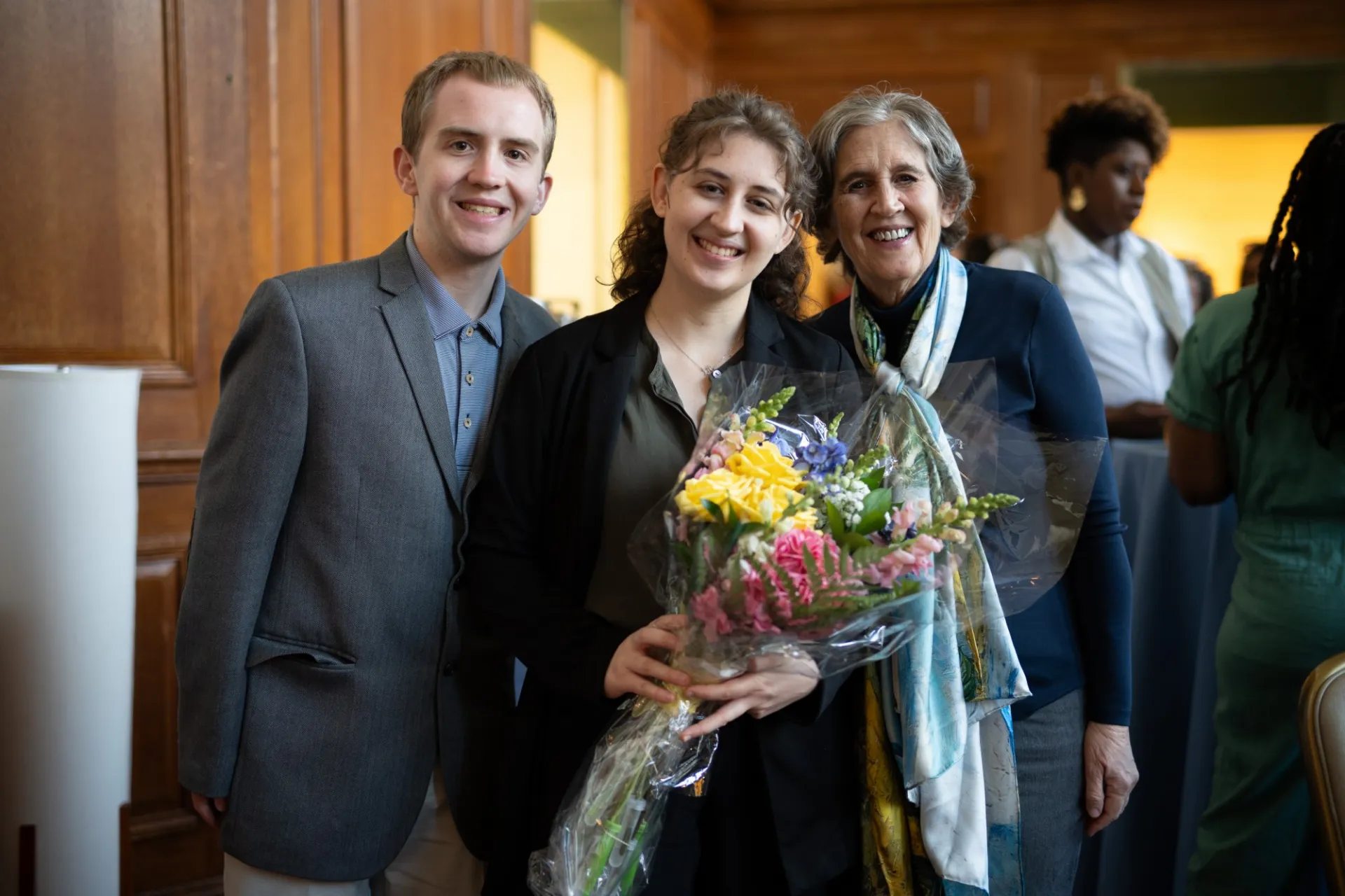 A woman holding a bouquet of flowers poses with two other people.