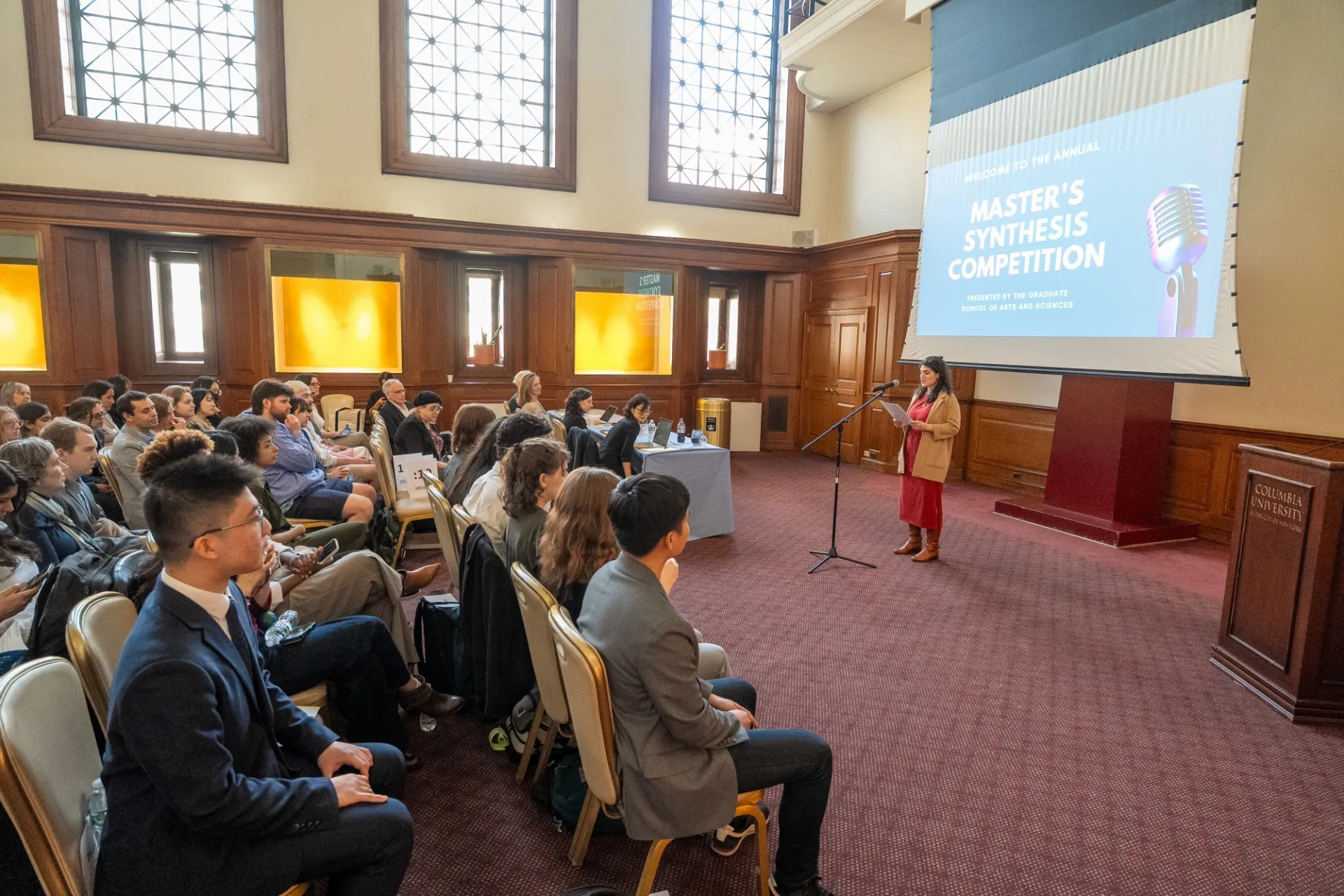 A woman speaking before a large audience of students and faculty.