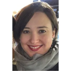 A woman wearing a thick scarf with brown hair smiles for a photo.