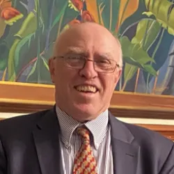 An elderly man wearing wire frame glasses and a formal suit smiles for a photo.