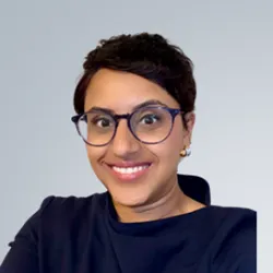A woman with brown hair, large round glasses, smiles at the camera.