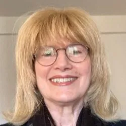 A woman with a blonde bob and round glasses smiles for a photo.