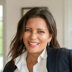 A woman in a blazer and brown hair smiles for a photo.
