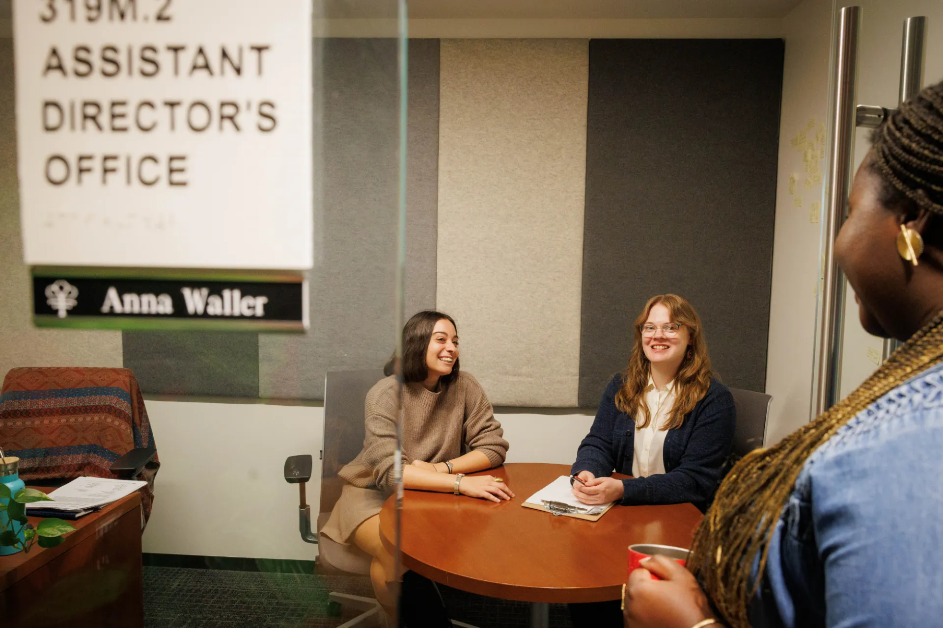 Students and employees gather laughing in the assistant director's office.