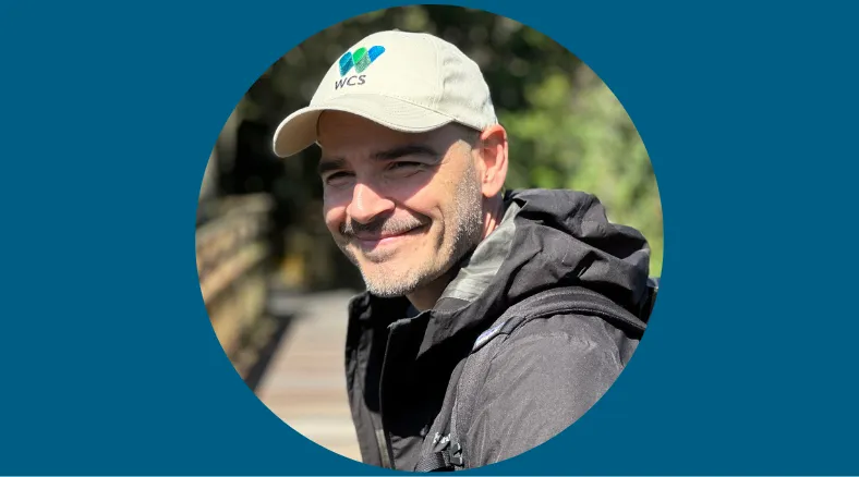 A man in a parka and a baseball cap smiles for a protrait.