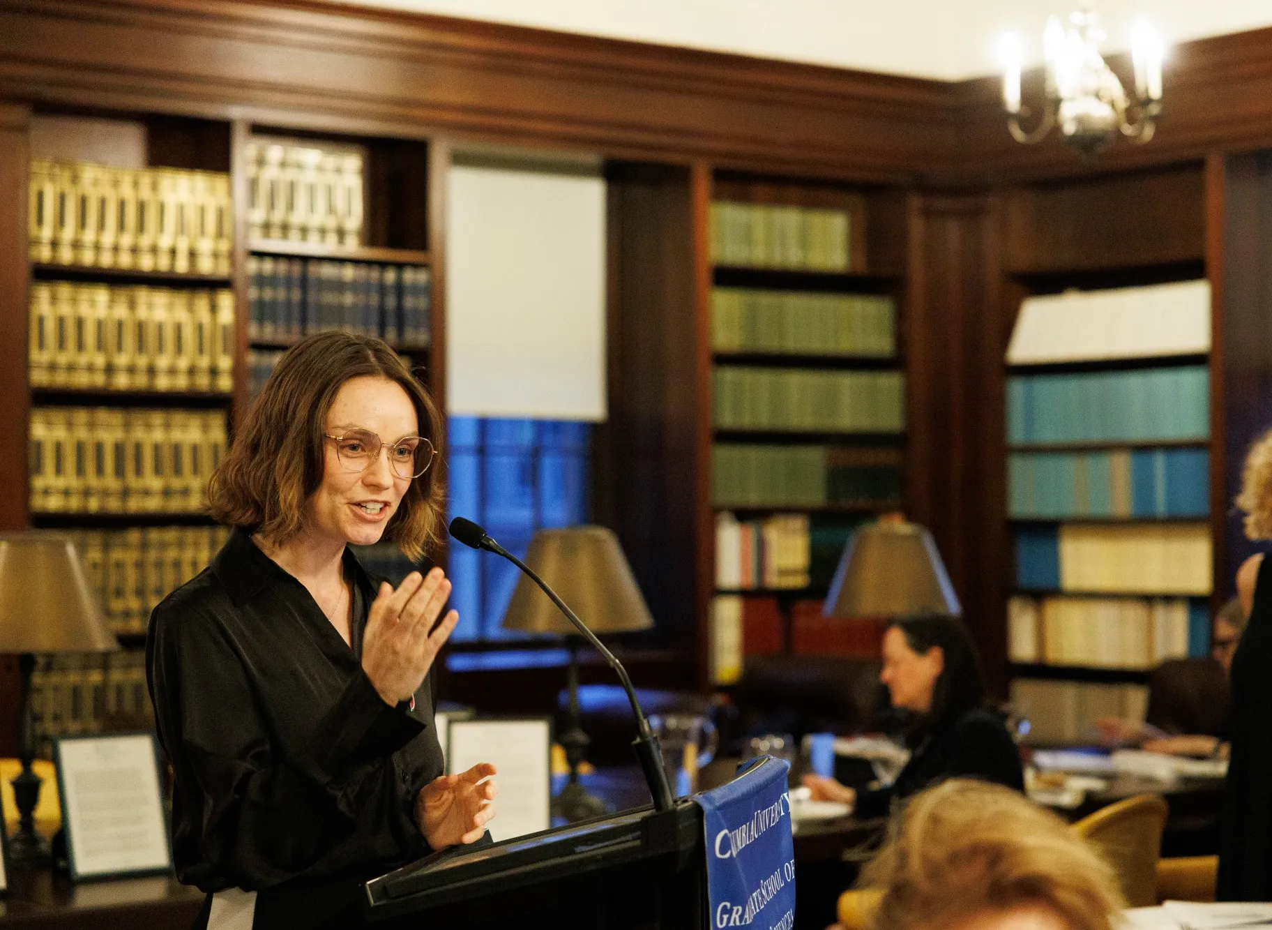 A woman at a lectern gesturing and speaking.