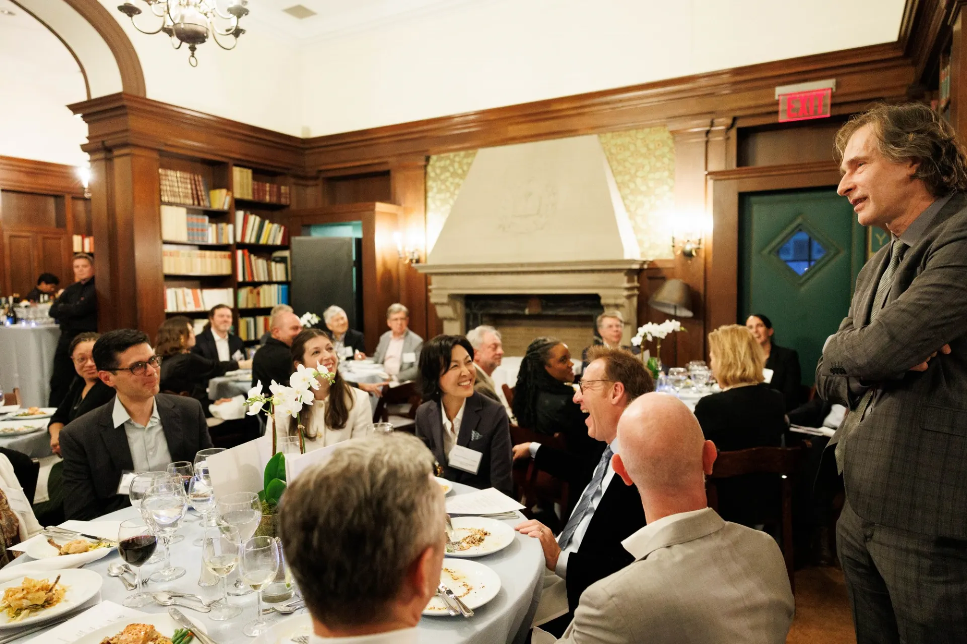 A group of people seated at a table, with a man chatting and standing beside them.