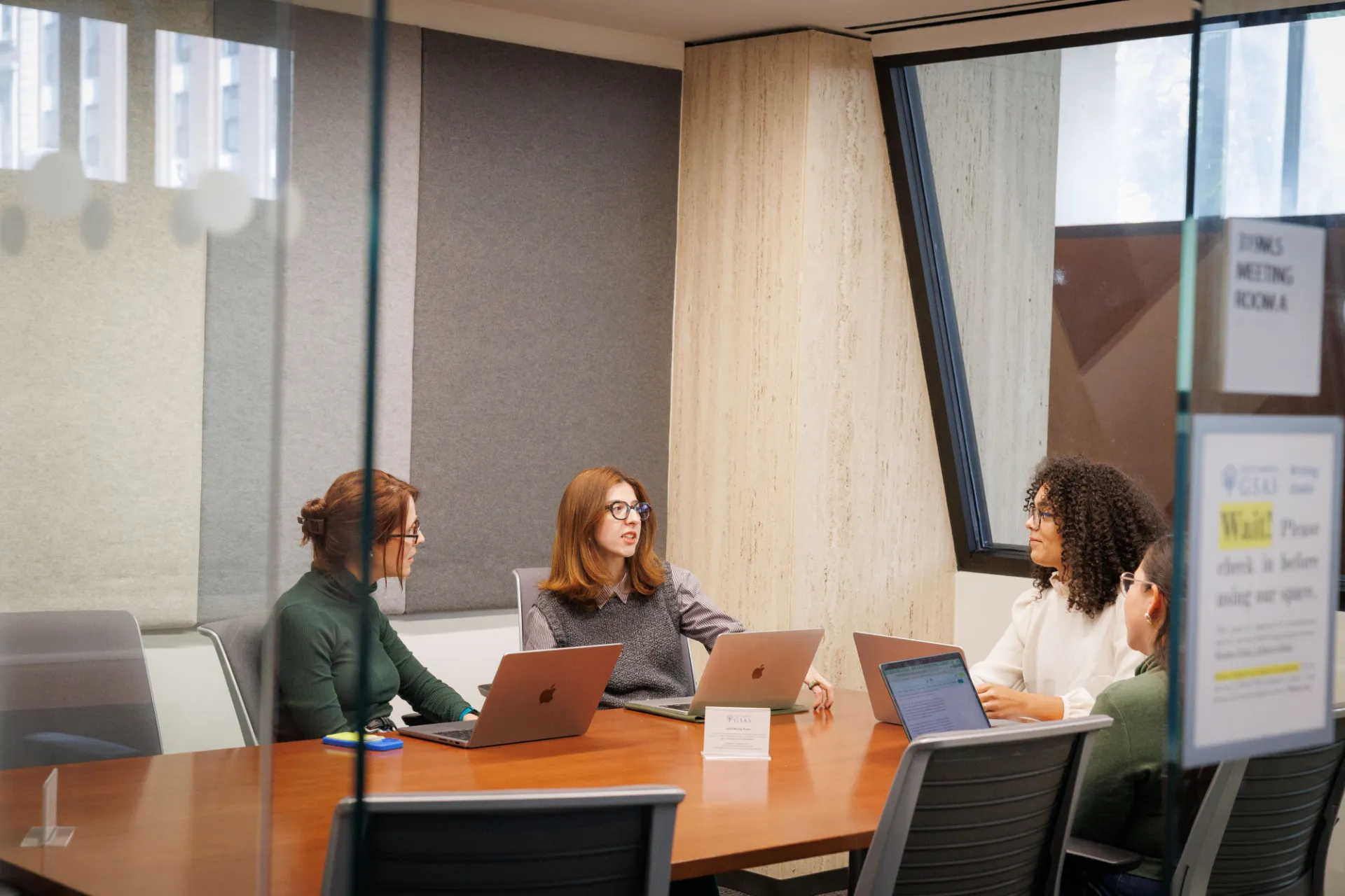 A group of students meet in a conference room, seated at a table, having a serious discussion.