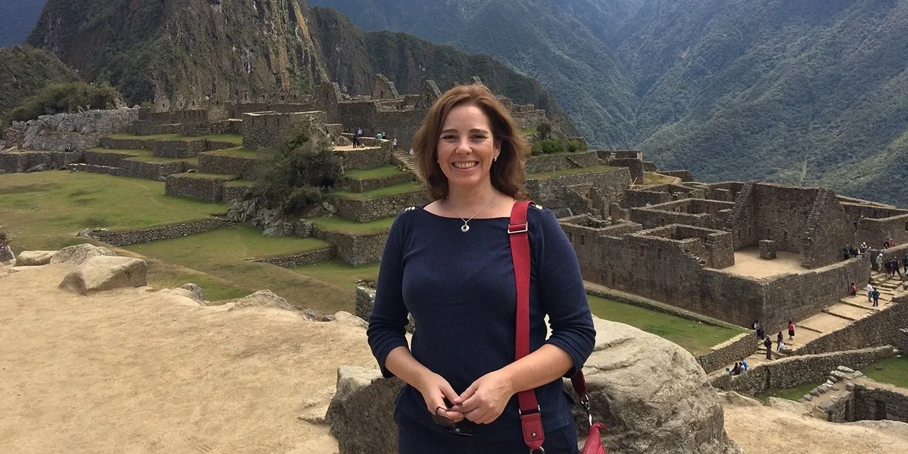 A woman smiles and poses in front of mountains and ancient ruins.