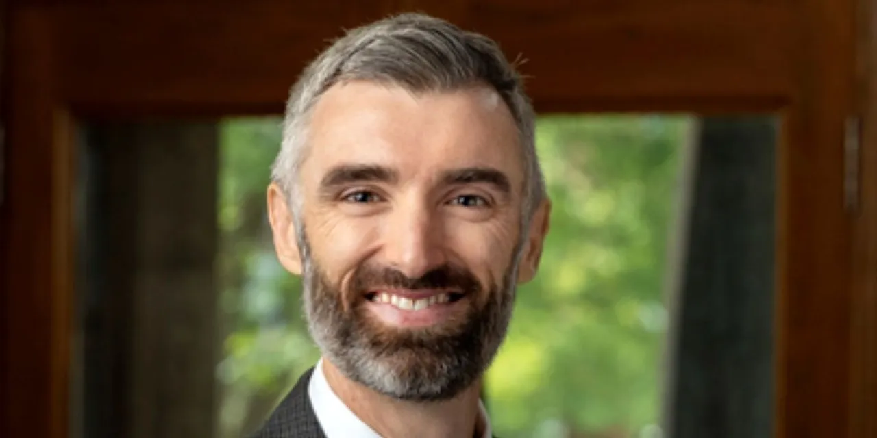 A headshot of a man with gray hair in a suit.