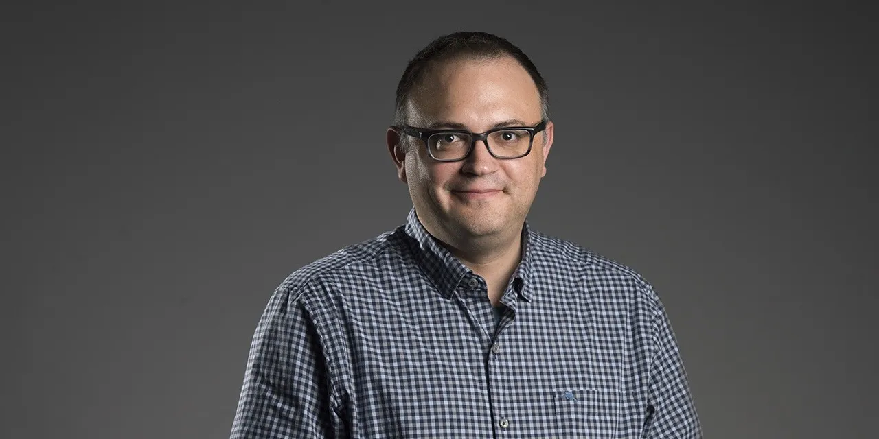 A portrait of a man in a button-up shirt wearing glasses.