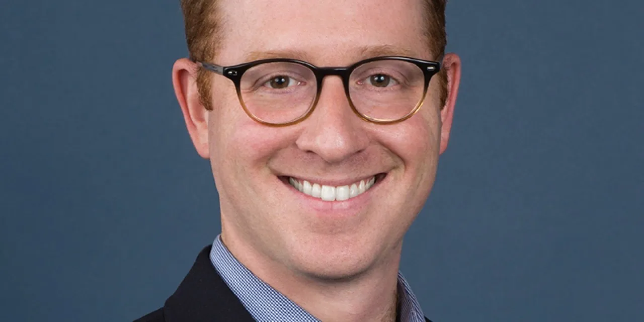 A headshot of a smiling man in a suit with glasses.