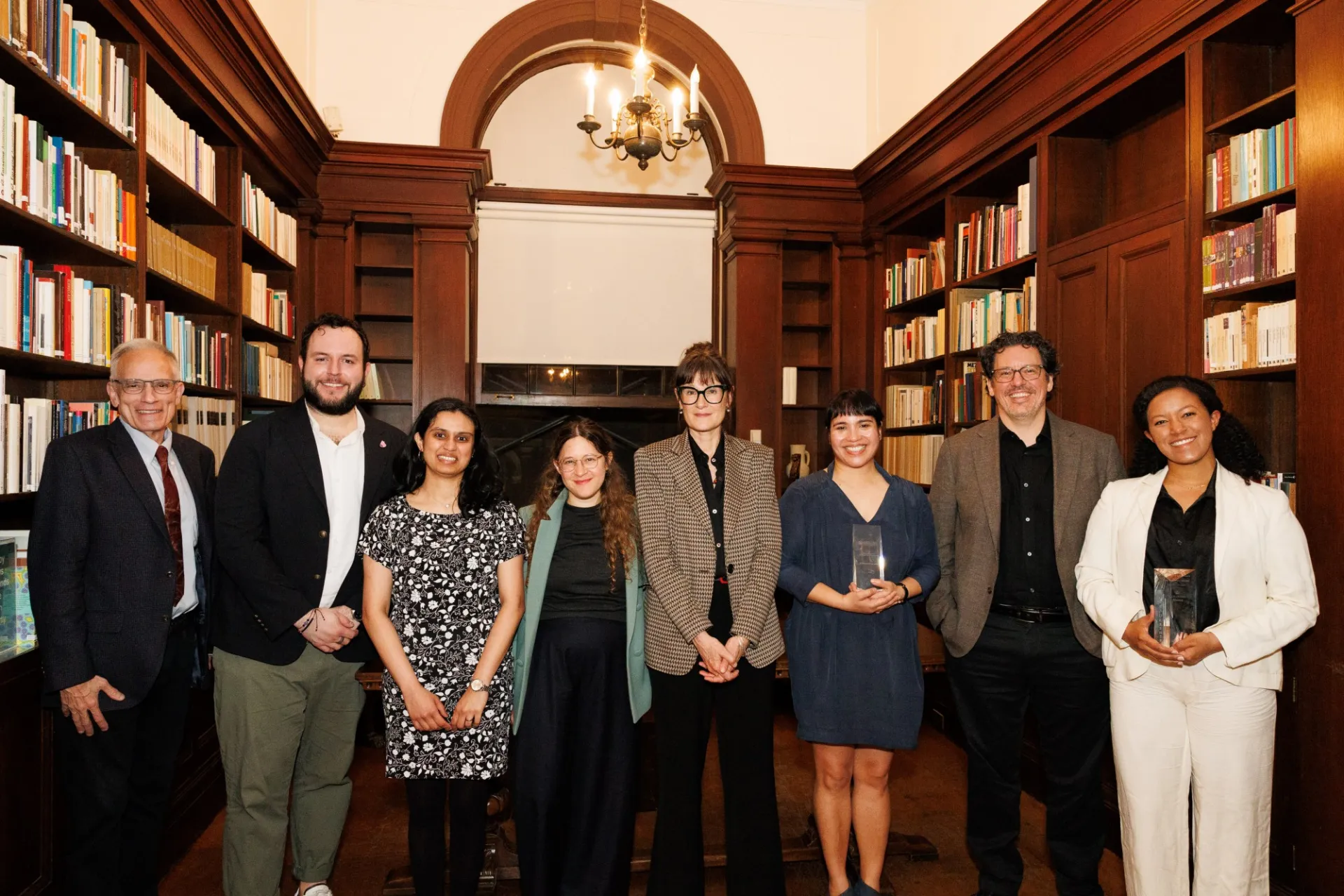 Eight men and women standing side-by-side smiling to camera. Some holding awards.