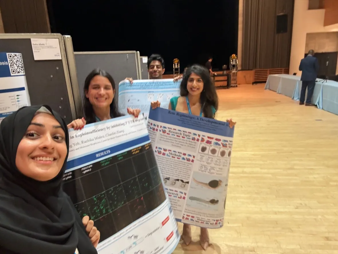 3 students at a symposium, holding up posters with research information