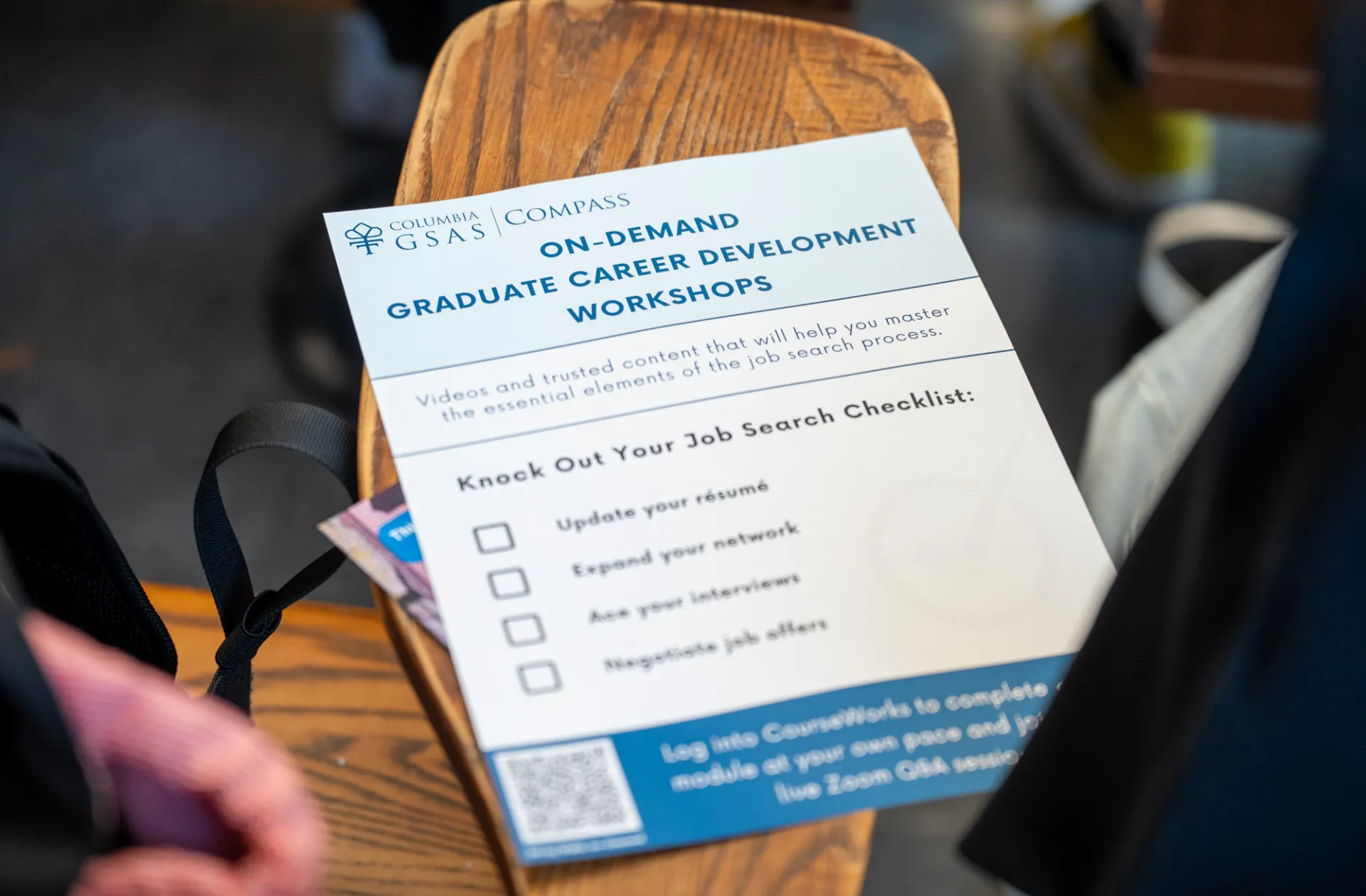 A flyer on a wooden bench promotes "On-Demand Graduate Career Development Workshops." It includes a job search checklist and a QR code, suggesting a focus on career advancement.