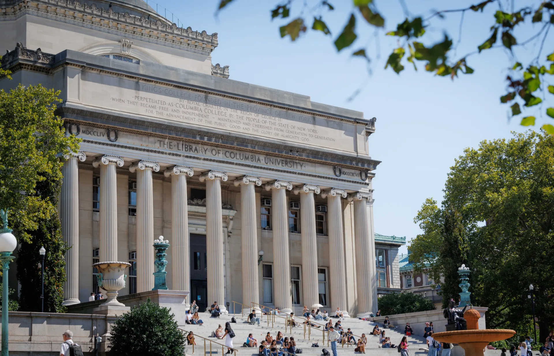 Low Library, a grand building with a large dome, massive columns, and steps. People sit on steps enjoying the sunny day, evoking a scholarly atmosphere.