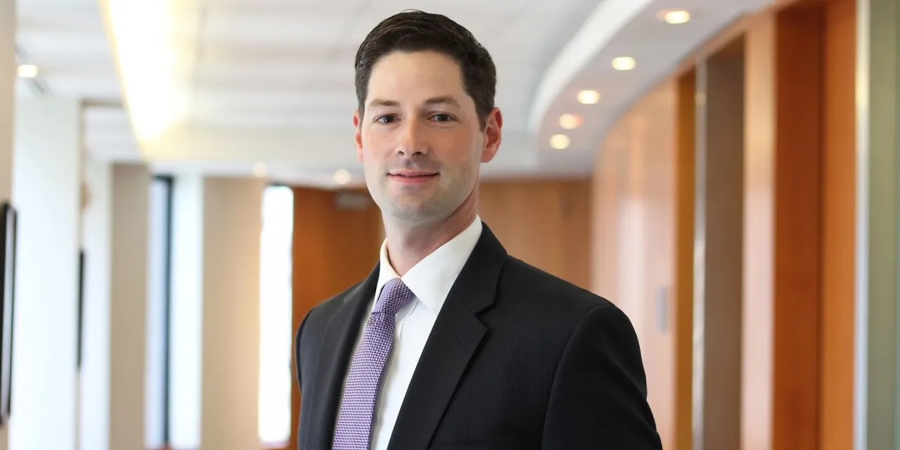 A portrait of a man in a suit in an office hallway.