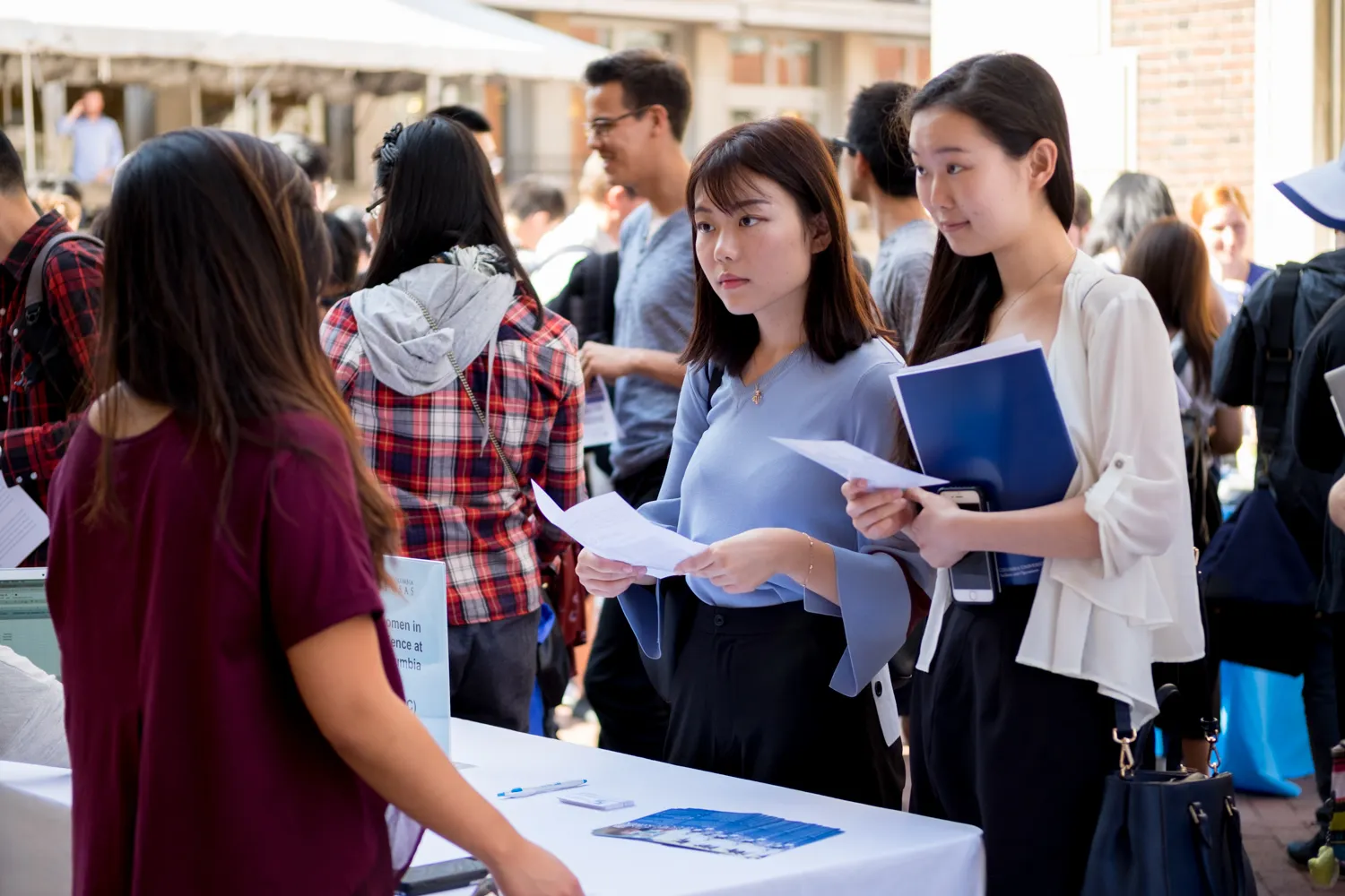 Two young women at a resource fair talking to someone at a booth.