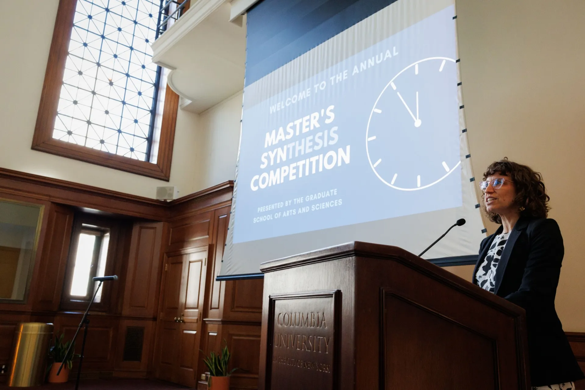 woman at lectern in from of slide presentation saying "MASTER'S SYNTHESIS COMPETITION"