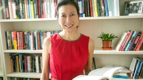 A woman in a red dress smiles in front of a bookshelf.