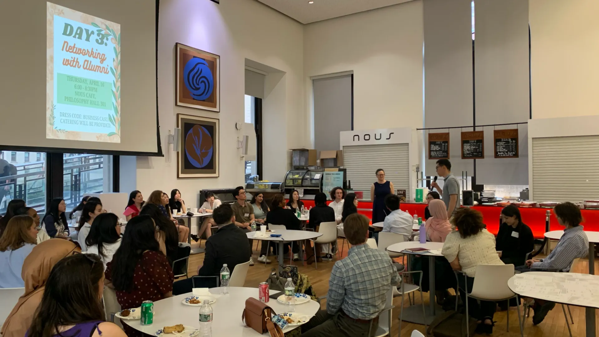 Students seated at tables in a coffee shop, a projector reads: Networking with Alumni.