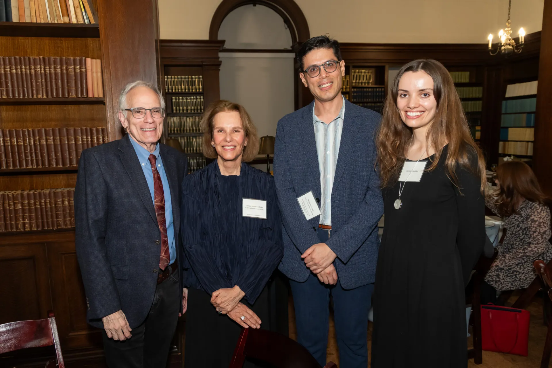 Four people in blazers smile in a wood-panelled room.