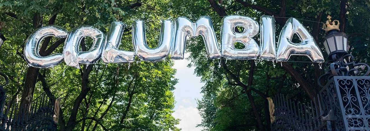 Silver balloons that spell out Columbia hang against trees on College Walk. 