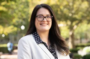 Woman with long brown hair and glasses smiling to camera